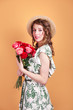 © Elena Kratovich - Portrait of attractive young woman in summer dress and straw hat holding roses bouquet on yellow background
