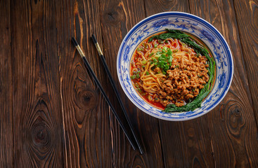 Wall Mural - Delicious and spicy homemade sichuan rice noodle in traditional blue bowl with black chopsticks on wooden table, asian food concept copy space for menu design