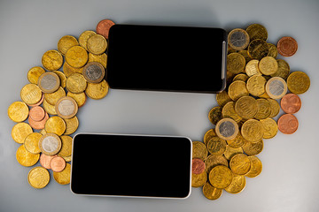 Two mobile phones and coins lie on a light background.