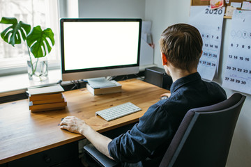 Man working from a home office. Computer with blank empty screen for copy space and information. A businessman from behind shoulder view. A creative entrepreneur