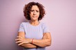 © Krakenimages.com - Middle age beautiful curly hair woman wearing casual t-shirt over isolated pink background skeptic and nervous, disapproving expression on face with crossed arms. Negative person.