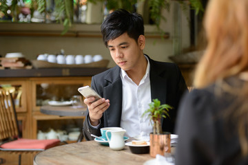 Young Asian business couple together at the coffee shop with man using phone