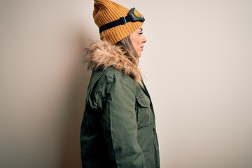 Poster - Young brunette skier woman wearing snow clothes and ski goggles over white background looking to side, relax profile pose with natural face and confident smile.