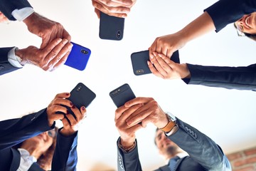 Group of business workers smiling happy and confident. Standing on a circle with smile on face using smartphone together at the office.