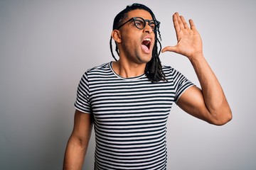 Wall Mural - Young handsome african american man with dreadlocks wearing striped t-shirt and glasses shouting and screaming loud to side with hand on mouth. Communication concept.