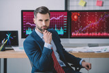 Fototapeta Kwiaty - Handsome data analyst looking at camera near charts on computer monitors on table in office