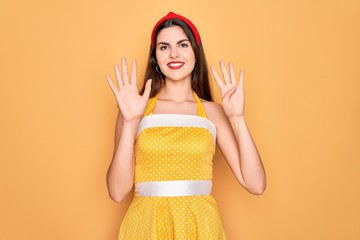 Poster - Young beautiful pin up woman wearing 50s fashion vintage dress over yellow background showing and pointing up with fingers number nine while smiling confident and happy.