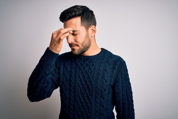 Wall Mural - Young handsome man with beard wearing casual sweater standing over white background tired rubbing nose and eyes feeling fatigue and headache. Stress and frustration concept.