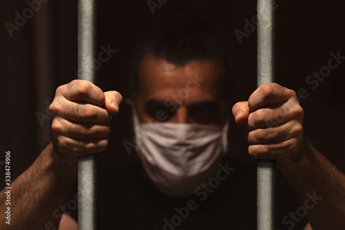Man with white medical mask standing in the dark, holding bars with his bare han Tableau sur Toile