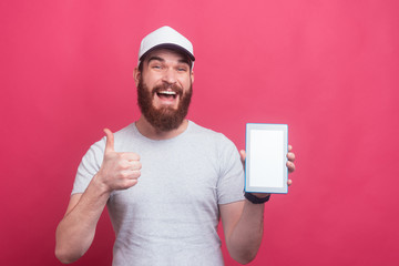 Portrait of amazed bearded man showing thumbs up gesture and tablet blank screen