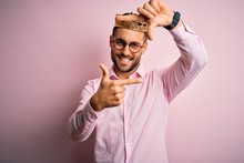 Young Handsome Business Man Wearing Golden Crown As King Over Pink Background Smiling Making Frame With Hands And Fingers With Happy Face. Creativity And Photography Concept.