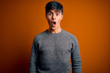 Sticker - Young handsome man wearing casual sweater standing over isolated orange background afraid and shocked with surprise and amazed expression, fear and excited face.