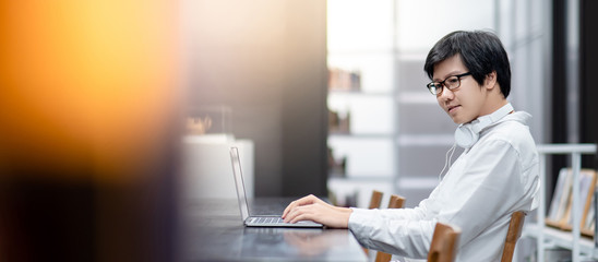 Asian man entrepreneur wearing glasses and headphones using laptop at home office. Businessman working with personal computer thinking about business project. Work smart with modern technology.