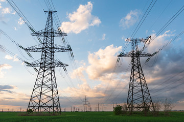 Wall Mural - high-voltage power lines passing through a green field, on the background of a beautiful cloudy sky