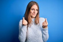 Young Beautiful Redhead Woman Wearing Casual Sweater Over Isolated Blue Background Doing Money Gesture With Hands, Asking For Salary Payment, Millionaire Business