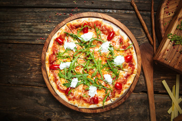 Wall Mural - Top view on italian cuisine dish fresh cooked pizza with tomatoes, mozzarella cheese and arugula on the dark wooden table, horizontal format