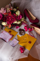 Wall Mural - wedding accessories: a bride’s bouquet of roses, peonies and hydrangeas, wedding rings on a stone, a ring and earrings with diamonds, women's shoes, invitation and yellow envelopes with a red wax seal