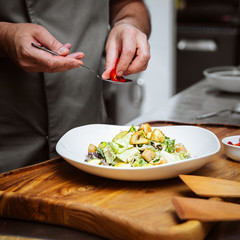 Sticker - Restaurant chef cooking warm salad with lettuce, mushrooms and potato on the wooden board in the kitchen, square format