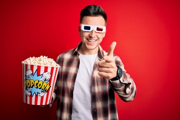 Wall Mural - Young handsome caucasian man wearing 3d movie glasses and eating popcorn pointing fingers to camera with happy and funny face. Good energy and vibes.