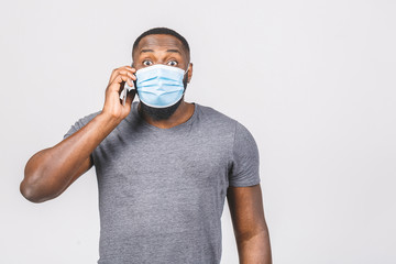 Shocked young african american man in sterile face mask posing isolated on white wall background. Epidemic pandemic coronavirus 2019-ncov sars covid-19 flu virus concept. Using phone.