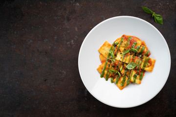 Cooked ravioli with tomatoes, pesto sauce and Basil leaves on a white plate, top view and copy space