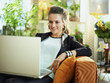 smiling modern woman using website while sitting on sofa