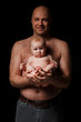 father holds a newborn son in his arms and looks at the camera A bald man with a naked torso and a 4-month-old baby