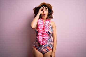 Sticker - Young beautiful arab woman on vacation wearing swimsuit and hawaiian lei flowers doing ok gesture shocked with surprised face, eye looking through fingers. Unbelieving expression.