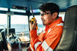 © Igor Kardasov - Filipino deck Officer on bridge of vessel or ship wearing coverall during navigaton watch at sea . He is speaking on portable GMDSS VHF radio, short range communication