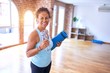 Middle age beautiful sportwoman smiling happy and confident. Standing with smile on face holding mat and bottle of water before doing exercise at gym