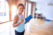 Middle Age Beautiful Sportwoman Smiling Happy And Confident. Standing With Smile On Face Holding Mat And Bottle Of Water Before Doing Exercise At Gym