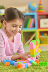 Wall Mural - Curly little girl playing with colorful plastic blocks