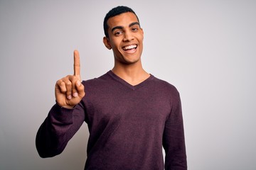 Young handsome african american man wearing casual sweater over white background showing and pointing up with finger number one while smiling confident and happy.