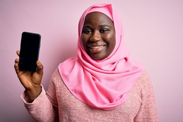 Sticker - African american plus size woman wearing muslim hijab holding smartphone showing screen with a happy face standing and smiling with a confident smile showing teeth