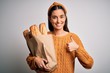 © Krakenimages.com - Young beautiful brunette woman holding paper bag with bread over white background happy with big smile doing ok sign, thumb up with fingers, excellent sign