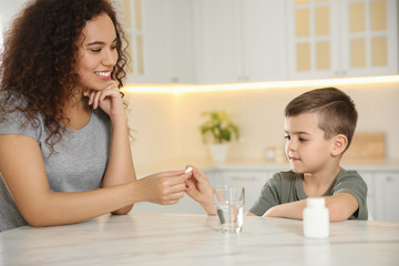 Poster - African-American woman giving vitamin pill to little boy in kitchen