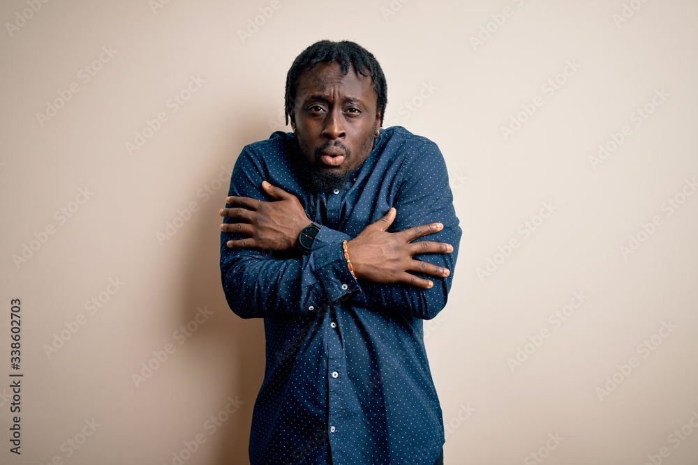 Young handsome african american man wearing casual shirt standing over white background shaking and freezing for winter cold with sad and shock expression on face