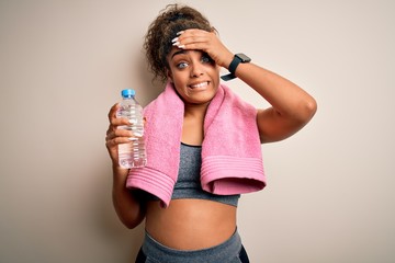 Canvas Print - Young african american sporty woman doing sport wearing towel drinking bottle of water stressed with hand on head, shocked with shame and surprise face, angry and frustrated. Fear and upset