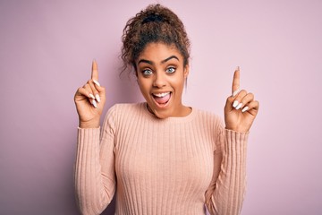 Sticker - Young beautiful african american girl wearing casual sweater standing over pink background smiling amazed and surprised and pointing up with fingers and raised arms.