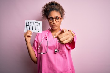 Poster - African american doctor girl wearing medical uniform and stethoscope holding help paper pointing with finger to the camera and to you, hand sign, positive and confident gesture from the front