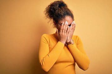 Poster - Young beautiful african american girl wearing sweater and glasses over yellow background with sad expression covering face with hands while crying. Depression concept.