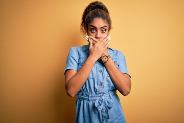 Sticker - Young beautiful african american girl wearing denim dress standing over yellow background shocked covering mouth with hands for mistake. Secret concept.