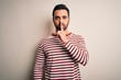 © Krakenimages.com - Young handsome man with beard wearing casual striped t-shirt standing over white background asking to be quiet with finger on lips. Silence and secret concept.