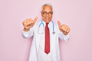 Wall Mural - Middle age senior grey-haired doctor man wearing stethoscope and professional medical coat approving doing positive gesture with hand, thumbs up smiling and happy for success. Winner gesture.