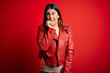 Sticker - Young beautiful woman wearing red leather jacket over isolated background looking stressed and nervous with hands on mouth biting nails. Anxiety problem.