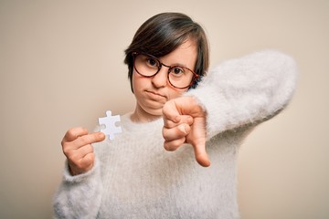 Sticker - Young down syndrome woman holding puzzle piece as problem solution and cooperation union with angry face, negative sign showing dislike with thumbs down, rejection concept