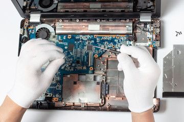 Man in white gloves holds screwdriver in his hands and repairs a laptop on a white background top view