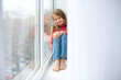 © cheese78 - girl sits on windowsill, near windowpane, she wants to walk on street, but in  world there is coronavirus pandemic, and she remains at home