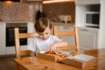 Wall Mural - The boy smiles and sorts dried fruits in a box sitting in the kitchen