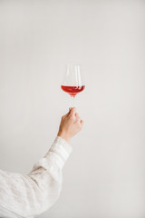 Womans hand holding glass of rose wine over white wall background. Wine shop, wine tasting, bar, wine list concept